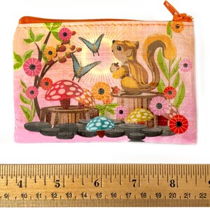 May include: A rectangular, zippered pouch with a whimsical illustration. The design features a squirrel holding an acorn, butterflies, mushrooms, and flowers in shades of pink, orange, and blue. The pouch has an orange zipper.
