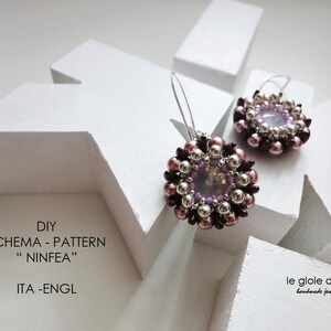 May include: A pair of handmade earrings with a purple and silver flower design. The earrings are made with small beads and a clear crystal in the center. The earrings are on a white background.