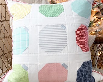 May include: Square decorative pillow with a white background and colorful geometric shapes. The shapes are in various colors, including yellow, green, blue, pink, and gray. The pillow has a red and white striped border.