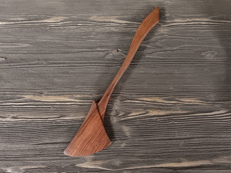 May include: A wooden spatula with a long, thin handle and a wide, flat blade. The spatula is made of dark wood and has a natural finish.