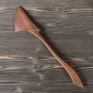 May include: A wooden spatula with a curved handle and a wide, flat blade. The spatula is made of dark brown wood and has a natural finish.