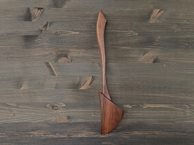 May include: A wooden spatula with a unique, curved design. The spatula is made of dark brown wood and has a smooth, polished finish.