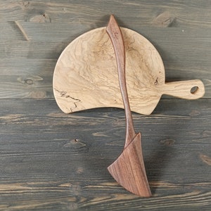 May include: A wooden serving spoon and a wooden cutting board with a natural wood grain pattern.