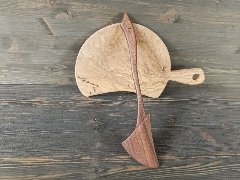 May include: A wooden serving spoon and a wooden cutting board with a natural wood grain pattern.
