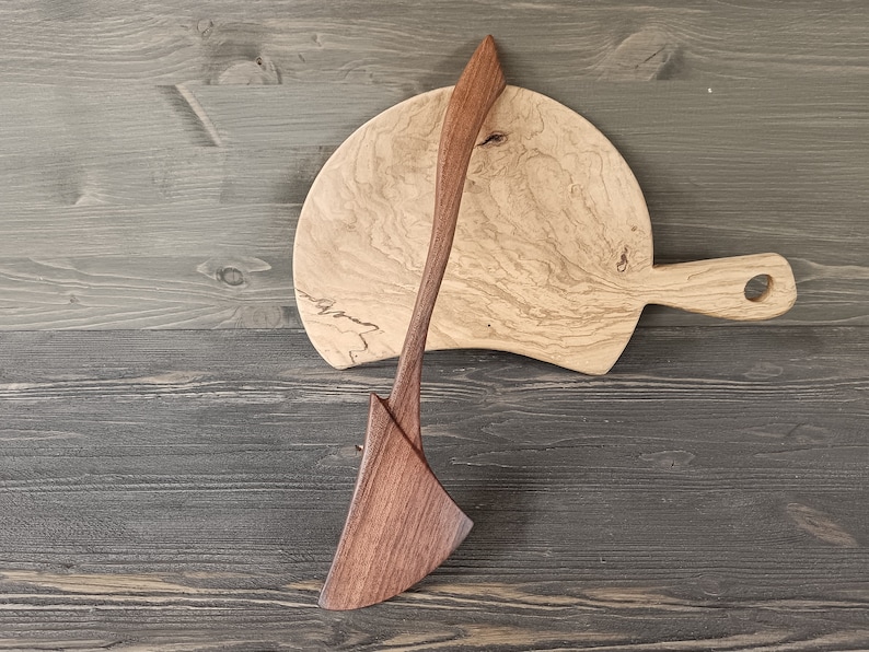 May include: A wooden serving spoon and a wooden cutting board with a natural wood grain pattern. The spoon is made of dark wood and the board is made of light wood.