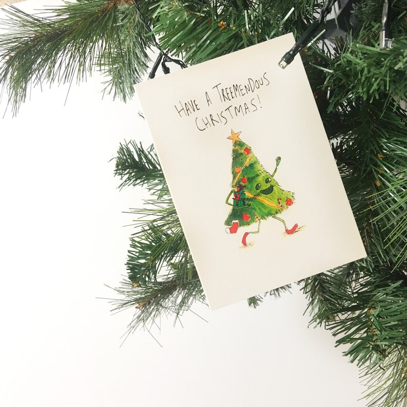 Puede incluir: Una tarjeta de Navidad con un &aacute;rbol de Navidad verde de dibujos animados con una cara sonriente y adornos rojos. El texto de la tarjeta dice "Have a Tremendous Christmas!"