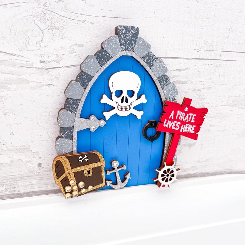 May include: A blue wooden fairy door with a skull and crossbones design, a treasure chest, an anchor, and a sign that reads "A pirate lives here".