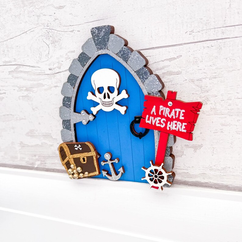 May include: A blue wooden fairy door with a skull and crossbones, a treasure chest, an anchor, and a steering wheel. A red sign reads "A Pirate Lives Here".