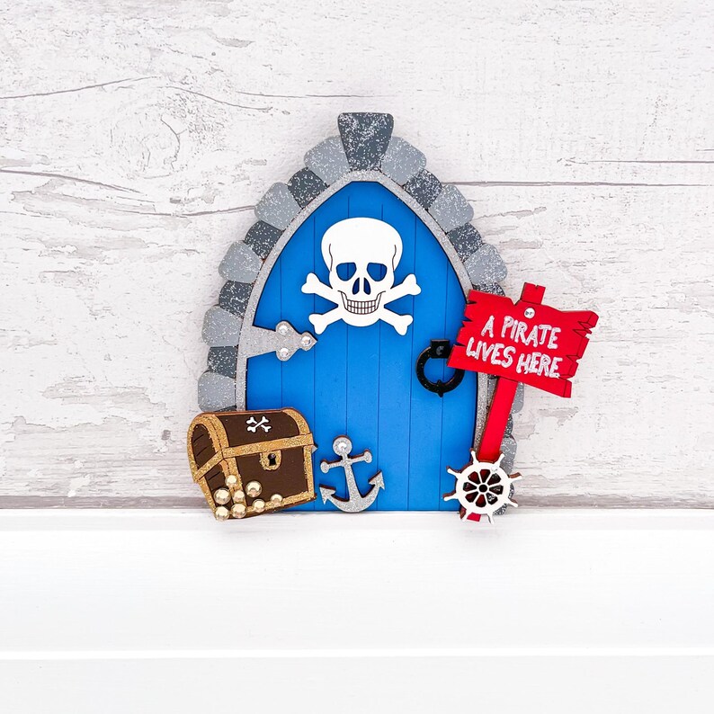 May include: A blue wooden fairy door with a skull and crossbones design, a treasure chest, an anchor, and a sign that reads "A pirate lives here".