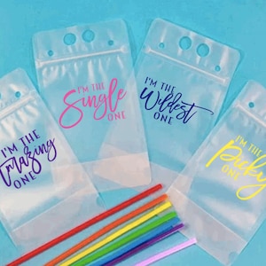 May include: Four clear plastic drink pouches with zipper closures and straw holes. Each pouch has a different colored text saying "I'm the Amazing One", "I'm the Single One", "I'm the Wildest One", and "I'm the Picky One".  A rainbow of straws is in the foreground.