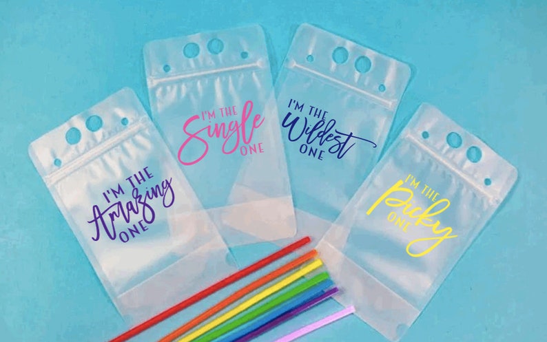 May include: Four clear plastic drink pouches with zipper closures and straw holes. Each pouch has a different colored text saying "I'm the Amazing One", "I'm the Single One", "I'm the Wildest One", and "I'm the Picky One".  A rainbow of straws is in the foreground.