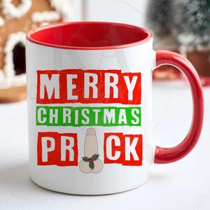 May include: A white ceramic mug with a red interior and handle. The front features the text MERRY in red, CHRISTMAS in green, and PRICK in red, with a phallic illustration replacing the letter I, decorated with a small green holly leaf graphic.