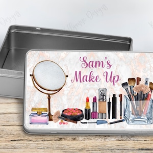 May include: A silver metal tin with a white marble design and the text "Sam's Make Up". The tin contains a variety of makeup items, including a mirror, lipstick, foundation, eyeliner, and brushes.