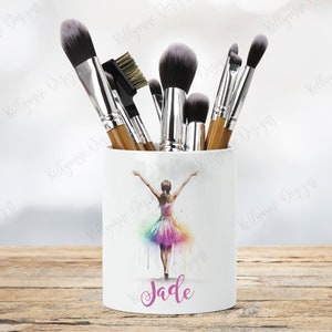 May include: White ceramic makeup brush holder with a watercolor illustration of a ballerina in a rainbow tutu. The name "Jade" is written in pink below the ballerina.