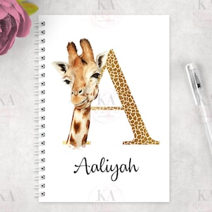 May include: A white spiral notebook with a gold letter A decorated with a giraffe print. The name Aaliyah is written in black cursive below the letter.