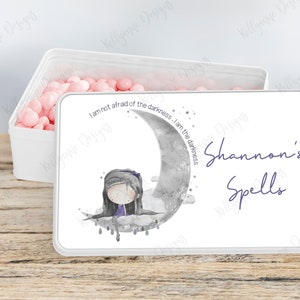 May include: White tin box with a pink and white design. The lid features a girl sitting on a crescent moon with stars and the text "I am not afraid of the darkness - I am the darkness". The bottom of the box has the text "Shannon's Spells" in purple.