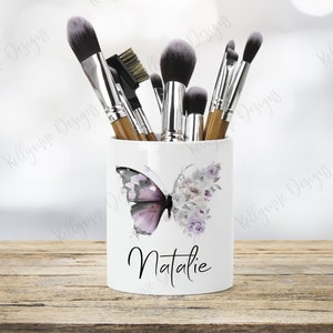 May include: White ceramic makeup brush holder with a watercolor butterfly and floral design. The holder has the name "Natalie" written on the front.