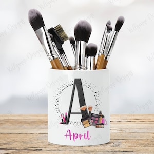 May include: White ceramic makeup brush holder with a black letter A and black polka dots. The holder has the name April written in pink letters below the letter A. The holder is filled with makeup brushes.