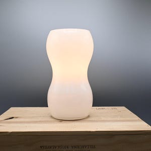 May include: A white ceramic table lamp with a rounded, hourglass-shaped base.