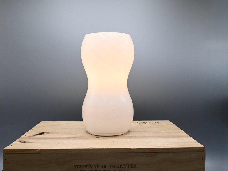 May include: A white ceramic table lamp with a rounded, hourglass-shaped base.