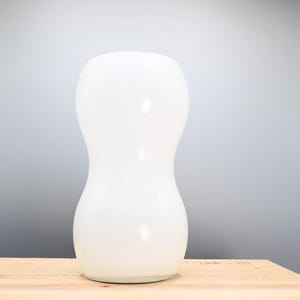 May include: A white ceramic vase with a rounded, hourglass shape. The vase is sitting on a wooden surface.