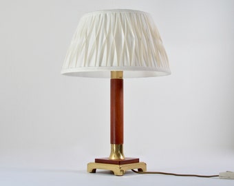 May include: A brass and wood table lamp with a white pleated lampshade. The lamp has a square base and a cylindrical stem.