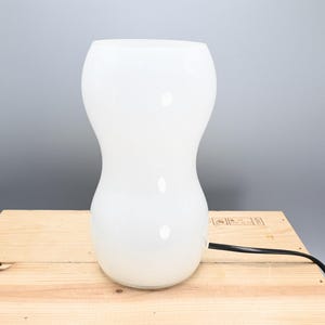 May include: A white ceramic table lamp with a rounded, hourglass-shaped base.