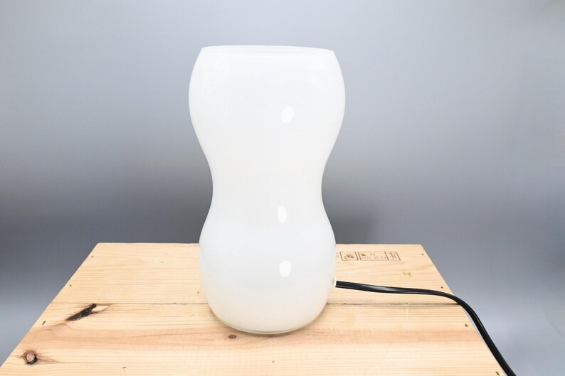 May include: A white ceramic table lamp with a rounded, hourglass-shaped base.