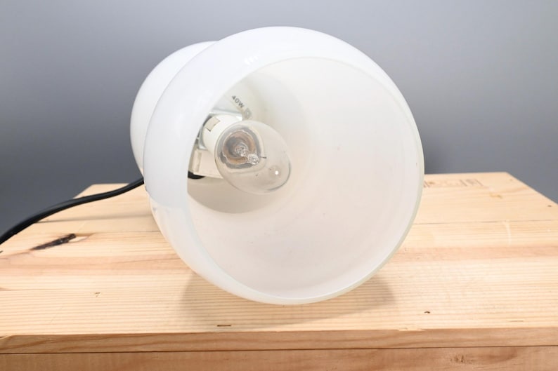 May include: White table lamp with a frosted glass shade and a black cord. The lamp is on a wooden surface.