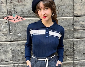 May include: A navy blue long-sleeved sweater with white stripes and a white collar. The sweater has a button-up closure and is worn with a black skirt and a black beret.