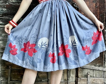 May include: A vintage-style skirt with a blue background and a floral pattern of red flowers and white circles. The skirt is paired with a red top and a red and white striped waistband. The skirt is knee-length.