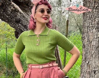May include: A woman wearing a green ribbed knit polo shirt with pink trim, a pink headband, and pink trousers. She is standing in front of a green leafy background.