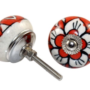 Puede incluir: Dos pomos de cajón de cerámica con fondo blanco y diseño floral rojo. Los pomos tienen un tornillo plateado y una base plateada.