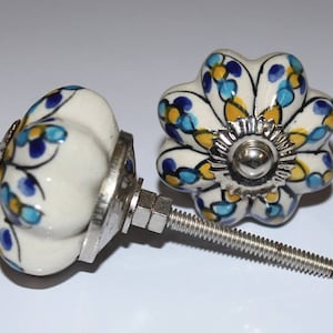 May include: Two white ceramic cabinet knobs with blue and yellow floral designs. The knobs have a silver metal base and screw.