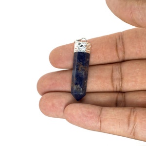 May include: A dark blue gemstone pendant with a silver cap, held in a hand.