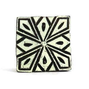 Könnte beinhalten: Ein quadratischer Holzblock mit einem geschnitzten Design einer geometrischen Blume in Schwarz und Weiß. Der Block wird zum Drucken von Mustern auf Stoff verwendet.