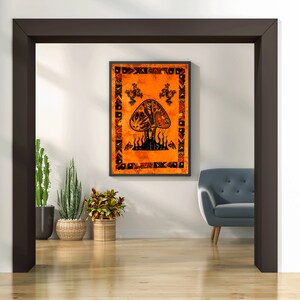May include: A tapestry with an orange background and a black and white mushroom design. The mushroom has a detailed design with a tree inside of it. The tapestry is framed and hanging on a white wall.