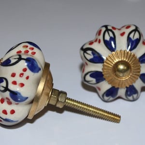 May include: Two ceramic cabinet knobs with a white base and blue and red floral designs. The knobs have a gold metal base and screw.