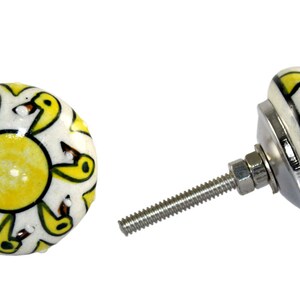 May include: Yellow and white ceramic knob with a sun and bird design. The knob has a silver screw.