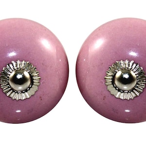 May include: Two round, pale purple cabinet knobs. Each knob features a silver-coloured, decorative base and a silver-coloured centre. These knobs are a decorative hardware item.