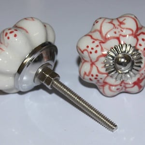May include: Two ceramic cabinet knobs with a white base and red floral designs. One knob has a silver screw and the other has a silver base.
