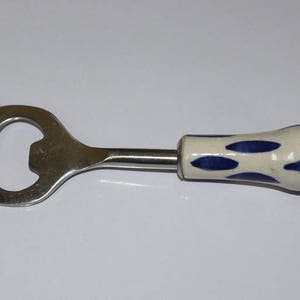 May include: A stainless steel bottle opener with a white ceramic handle decorated with blue spots.