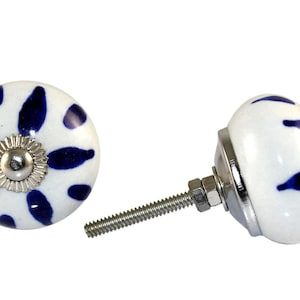 Pode incluir: Botão de cerâmica branco com um design floral azul e um parafuso prateado. O botão é redondo e tem um centro elevado.