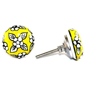 May include: Two yellow ceramic cabinet knobs with white floral designs and black outlines. Each knob has a metal base and a threaded rod for installation. The knobs are set against a white background.
