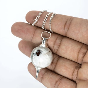 May include: A silver chain with a white and black crystal pendulum. The pendulum is round and has a pointed tip.
