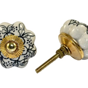 Op de afbeelding: Witte keramische kastknop met een zwart bloemenontwerp en een gouden midden. De knop heeft een gouden schroef.