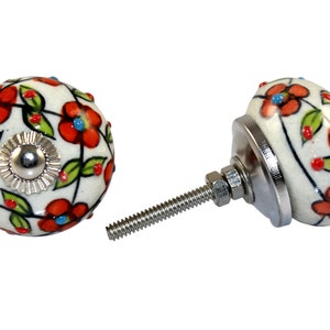 May include: A pair of white ceramic cabinet knobs with a floral design featuring red, green and blue accents. The knobs have a silver screw and a silver base.
