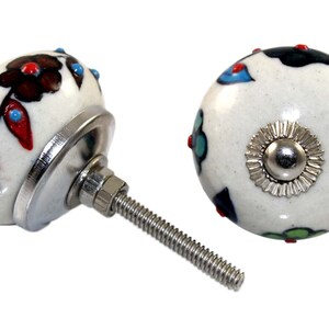 Puede incluir: Dos pomos de armario de cerámica blanca con un tornillo de metal plateado. Los pomos están decorados con patrones florales coloridos y tienen una base de metal plateado.