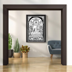 May include: Black and white line art print of a Buddha sitting in meditation with a halo and surrounded by other figures. The print is framed and hanging on a white wall in a room with a grey sofa and potted plants.