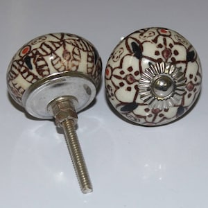 May include: Two ceramic door knobs with a white background and intricate brown and red floral patterns. One knob has a silver screw and the other has a silver base.